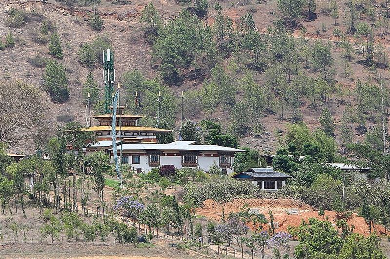 ブータンの山の斜面に建つ寺院チミ・ラカンの遠景。黄金色の屋根と白い建物が木々に囲まれている