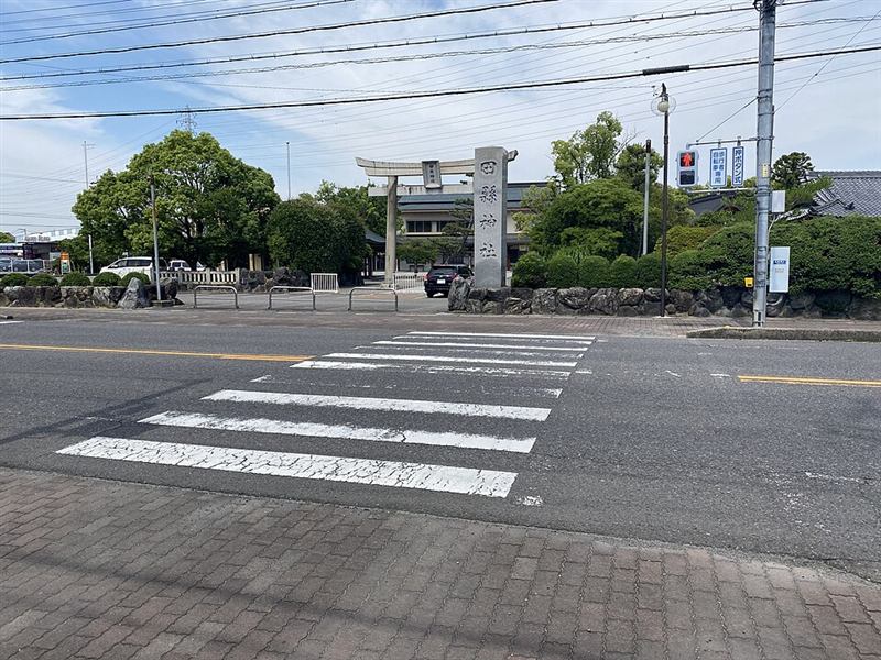 田縣神社の入口。道路の向こうに鳥居と「田縣神社」と刻まれた石の社号標が立っている